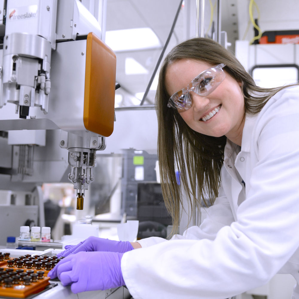 A young woman researcher in the lab, smiling at the camera.